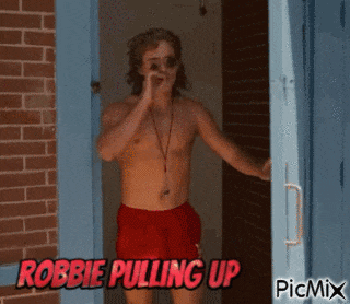 a shirtless man in red shorts is standing in front of a brick wall with the words robbie pulling up on the bottom