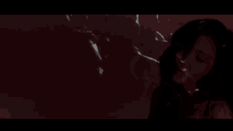 a close up of a woman 's face in a dark room with a projection of her face on the wall .