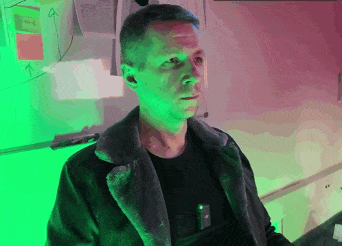 a man in a black jacket stands in front of a white board with sticky notes on it