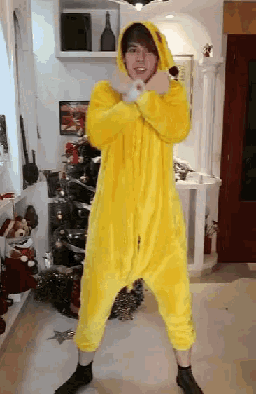 a person in a yellow onesie is dancing in front of a christmas tree