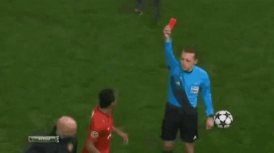 a soccer player in a red shirt is holding his head while a referee stands behind him .
