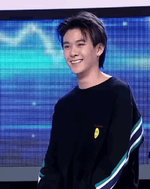 a young man wearing a black sweater with a smiley face on the back is smiling .