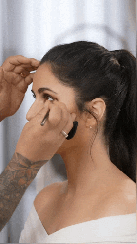 a woman is getting her makeup done by a man with tattoos