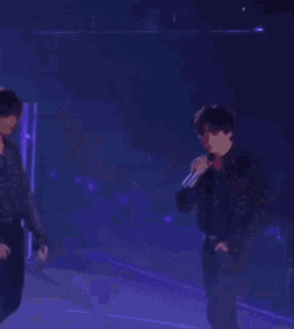 a group of men are standing on a stage holding microphones and dancing .