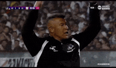 a man is raising his arms in the air while watching a soccer game .
