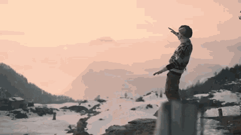 a man is standing on top of a snow covered mountain pointing to the sky .