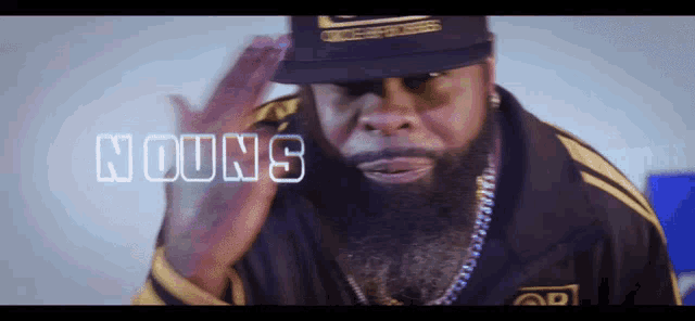 a man with a beard wearing a hat and a jacket that says nouns