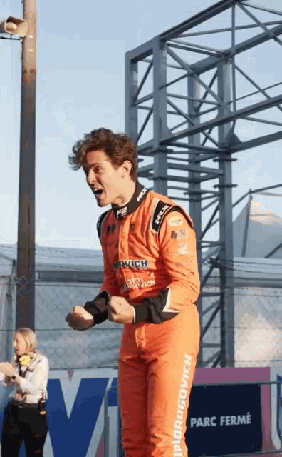 a man in an orange racing suit is standing in front of a sign that says " parc ferme "