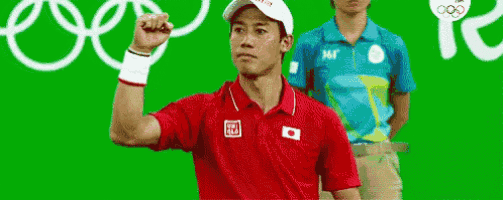 a man in a red shirt is raising his fist in the air in front of a green screen .