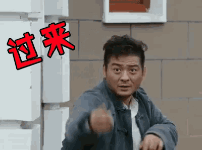 a man in a blue jacket is pointing at the camera with chinese writing on the wall behind him .
