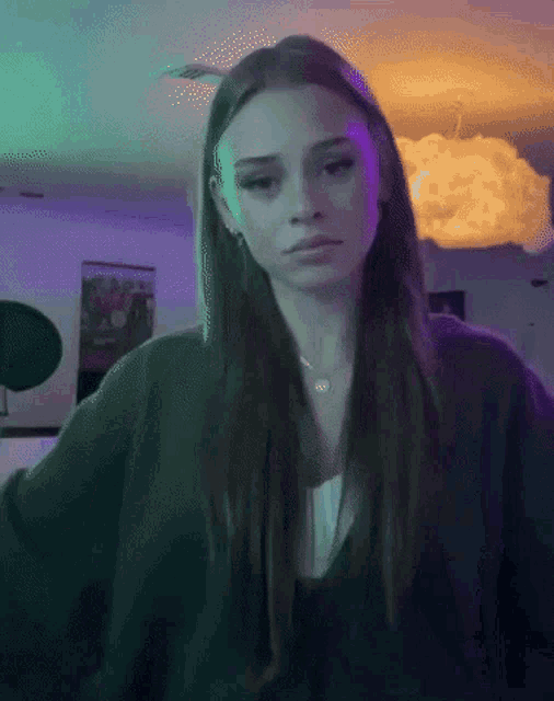 a woman with long brown hair is standing in a room with a purple light behind her