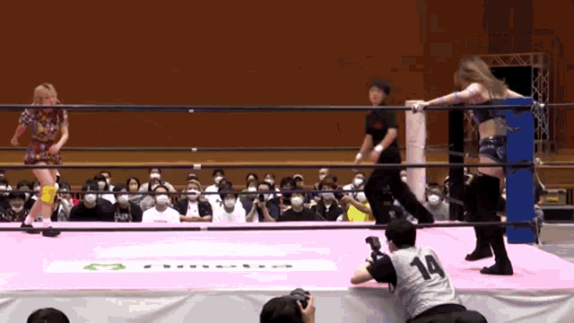 two women are wrestling in a ring with a referee wearing a number 14 shirt