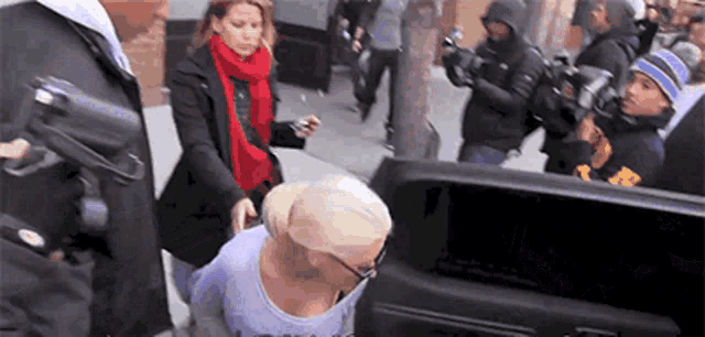 a woman in a purple shirt is being escorted into a car by a group of people