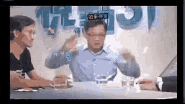 a man is sitting at a table with a glass of water in front of him and talking to another man .