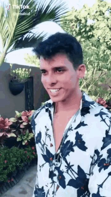 a young man wearing a floral shirt is smiling while standing in front of a palm tree .