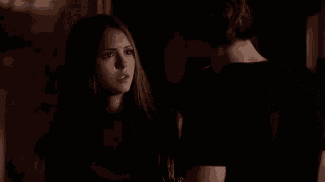 a man and a woman are standing next to each other in a dark room looking at each other .