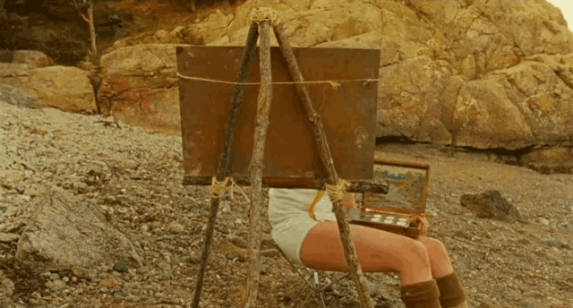 a woman is sitting in front of an easel with a painting on it