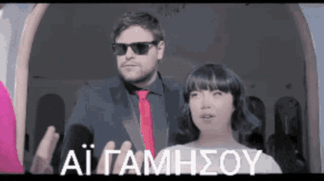 a man wearing sunglasses and a red tie stands next to a woman with the words ai gamhsou written on the bottom