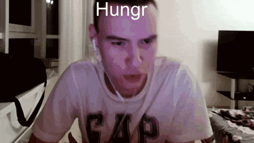 a man wearing a gap shirt is looking at the camera with the words hungr written on his face .
