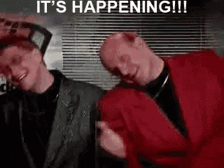 two men are standing next to each other in a room and laughing .