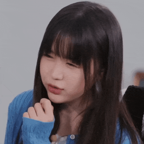 a girl with long hair and a blue sweater is making a funny face