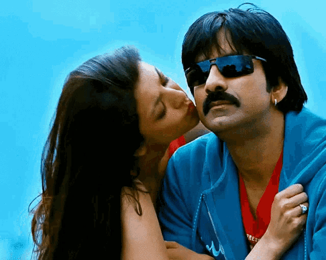 a woman kisses a man on the cheek while wearing sunglasses