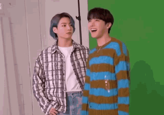 two young men are standing next to each other on a green screen .