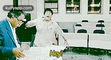 a man in a suit is standing next to a man in a white shirt who is holding a piece of paper that says hey