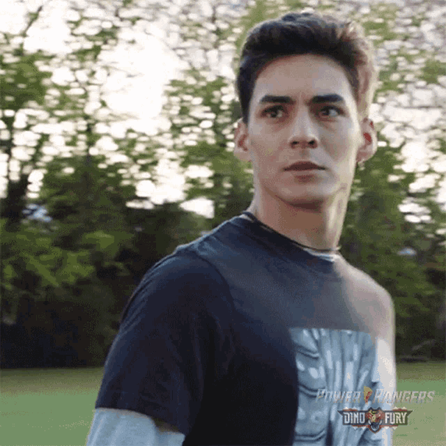 a young man wearing a black power rangers shirt stands in a field