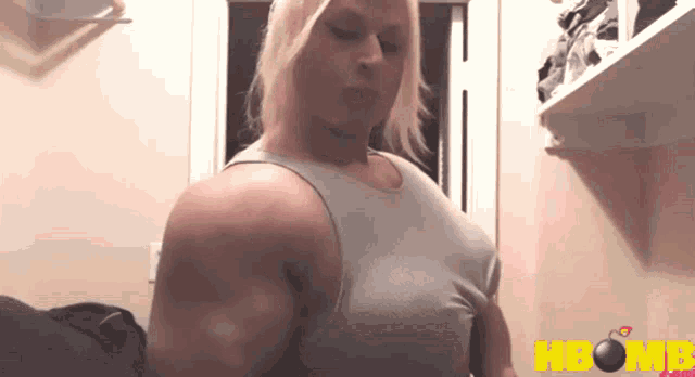 a woman in a tank top is standing in front of a shelf that says hbomb.com on it