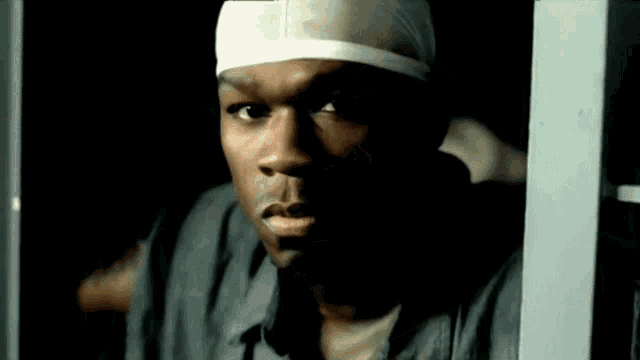 a man with a bandana on his head is behind bars in a dark room .