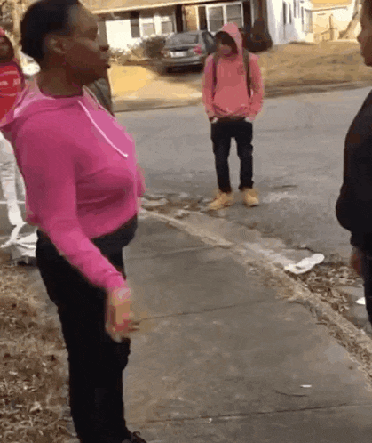a woman in a pink sweatshirt is standing on a sidewalk