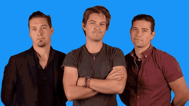 three men standing next to each other with their arms crossed against a blue background