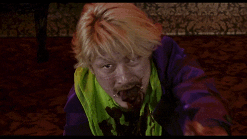 a man with blood on his face is wearing a green scarf and a purple shirt