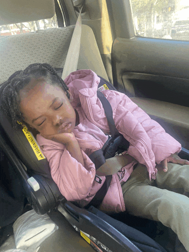 a little girl sleeping in a car seat with a yellow warning sign