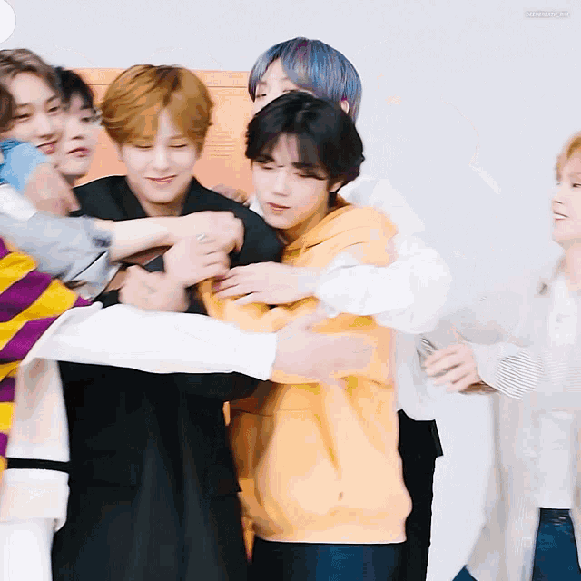 a group of young men are hugging each other and one of them is wearing an orange sweatshirt