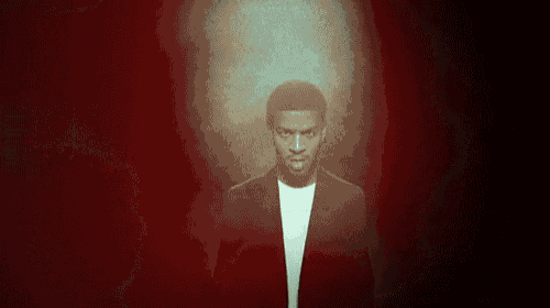 a man in a suit and white shirt is standing in a dark room with a red background .