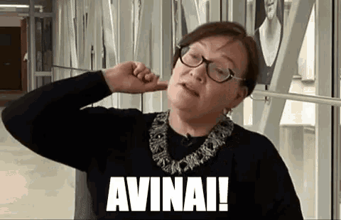 a woman wearing glasses and a black sweater is covering her ears with her hand and making a funny face .