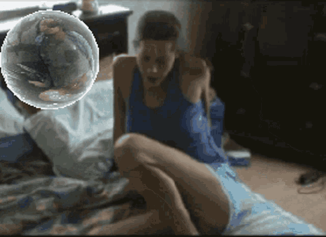 a woman in a blue tank top is sitting on a bed
