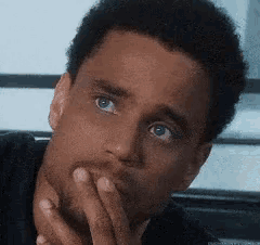 a close up of a man 's face with his hand to his mouth .