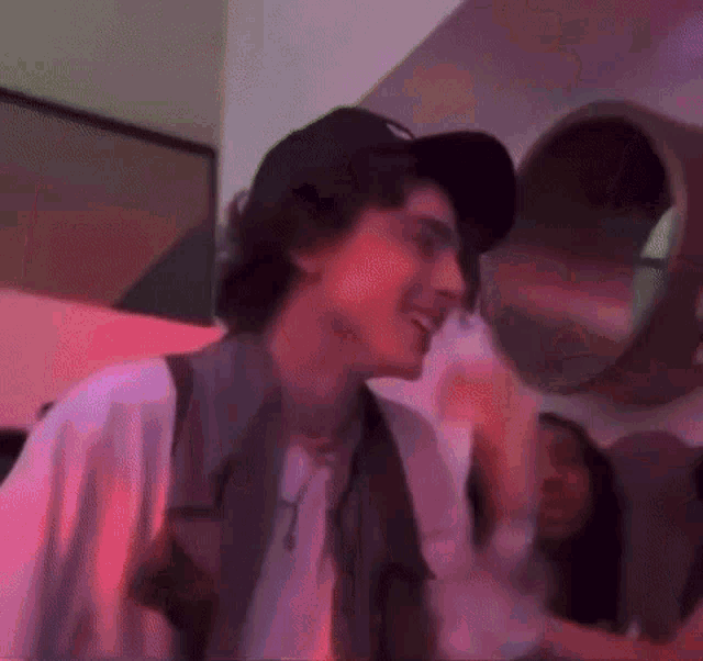 a man wearing a hat and a white shirt is standing in a room with pink lights .