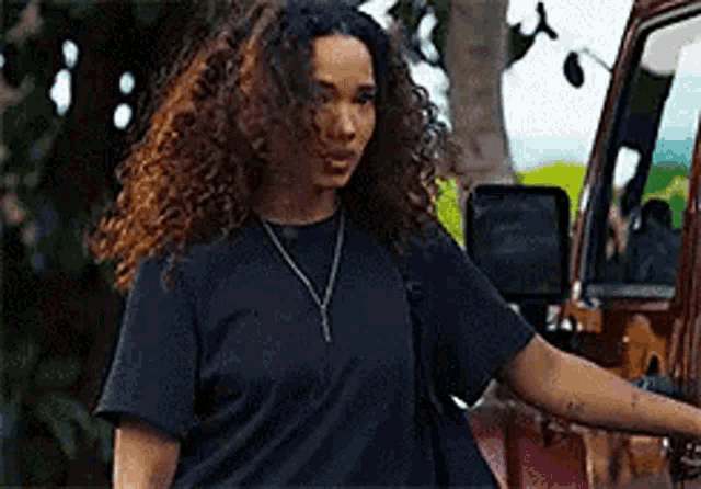 a woman with curly hair is standing next to a red car .