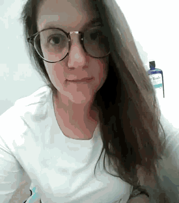 a woman wearing glasses and a white shirt is making a funny face