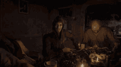 two men are sitting at a table in a dark room with candles on it .