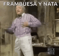 a man in a purple sweater and white pants is dancing in a room with his hands on his chest .