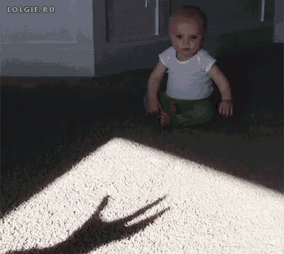 a baby is sitting on the floor and looking at his shadow on the floor .