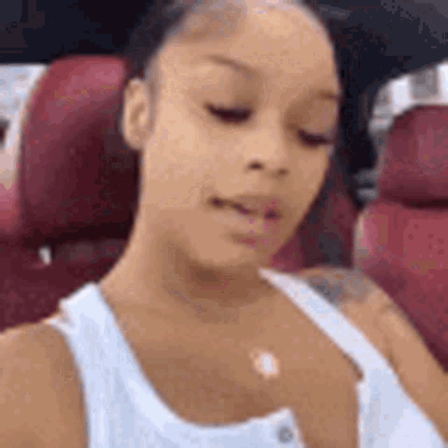 a woman in a white tank top is sitting in a car taking a selfie .