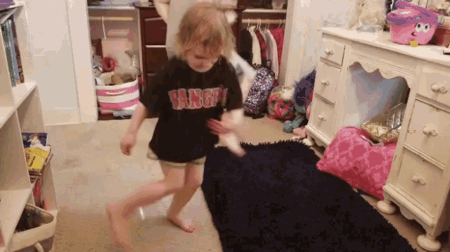 a little girl wearing a shirt that says varsity is dancing in a room