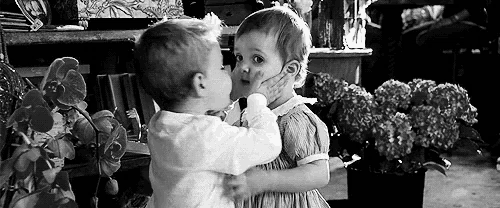 a black and white photo of a boy and a girl kissing .