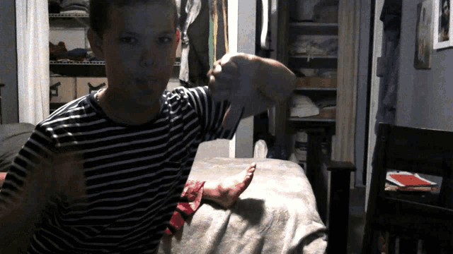 a boy in a striped shirt is sitting on a bed holding a white object